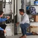 Two technicians working on an HVAC unit in a garage, with organized tools nearby, from Chad's AC Direct in Montgomery, AL.