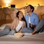 Couple enjoying a cozy movie night with popcorn and remote, reflecting relaxation in Chad's AC Direct service area.