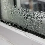 Close-up of a window with condensation, showing water droplets on the glass and frame, highlighting HVAC comfort issues.