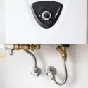 Water heater mounted on a wall with control knob and piping, part of Chad's AC Direct HVAC services in Montgomery, AL.