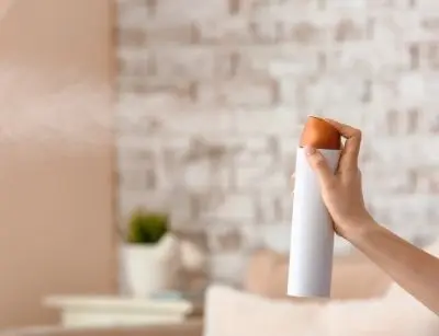 Person holding aerosol spray can in a home setting, illustrating potential source of volatile organic compounds (VOCs) affecting indoor air quality.
