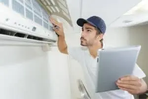 HVAC technician inspecting air conditioning unit while holding a tablet, representing air conditioning maintenance services.