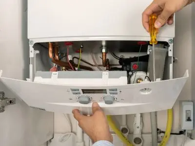 Person using a screwdriver to inspect the interior of a boiler, highlighting maintenance practices for efficient operation and leak prevention.