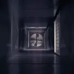Vertical view into an air duct shaft with a circular fan and dark metal surfaces, showcasing HVAC systems.