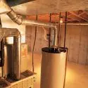Industrial hot water heater and boiler in basement HVAC room with metal pipes and concrete walls.