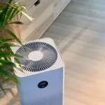 Air purifier with modern design and fan grill, surrounded by wooden furniture and an indoor plant, promoting healthy living.