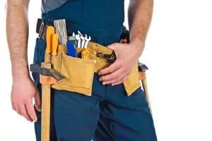 Person wearing work overalls with a tool belt, featuring various tools like a hammer, screwdrivers, and pliers, emphasizing maintenance and repair skills relevant to HVAC services.