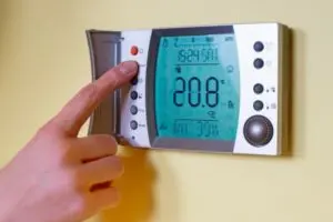 Digital thermostat displaying temperature settings with a hand adjusting controls, relevant to HVAC energy efficiency tips.