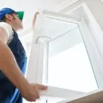 Worker installing a white window frame in a clean setting, emphasizing craftsmanship related to HVAC services.
