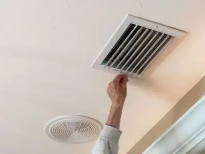 Person adjusting a ceiling air vent, demonstrating central air conditioning maintenance in a residential setting.