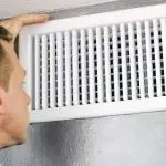 Man performing HVAC maintenance on a white air vent, ensuring efficient operation of Chad's AC Direct systems.