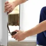 A person measuring a window frame with a tape measure for home improvement and HVAC installation.