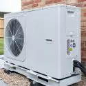 Air conditioning unit installed outdoors near a brick wall, featuring a fan and compressor on a base for HVAC services.
