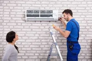 AC technician installing air conditioning unit on wall while homeowner observes, emphasizing HVAC services and professional installation for improved comfort and air quality.