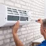 Technician performing maintenance on a wall-mounted air conditioning unit, emphasizing HVAC service expertise.