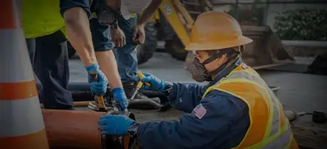 Plumber in safety gear working on drainage system, emphasizing professional drain cleaning services for plumbing maintenance and emergency prevention.