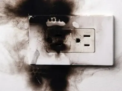 Damaged electrical outlet with burn marks and discoloration, illustrating the dangers of power surges in homes.