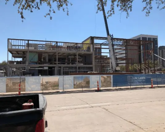 Construction progress of the Barbara & George H.W. Bush Convention Center in Midland, Texas, featuring steel framing and construction equipment, with Lee Lewis Construction branding visible on site fencing.