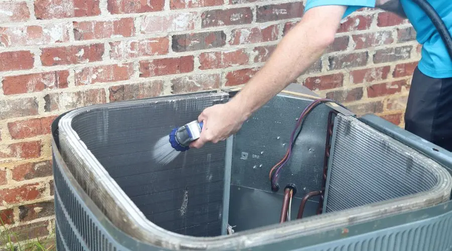 Technician cleaning air conditioning unit for indoor air quality at The Bosworth Company, with grass and brick wall backdrop.