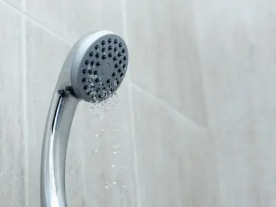 Showerhead with water flowing, illustrating poor water pressure issues related to plumbing problems and potential need for repiping.