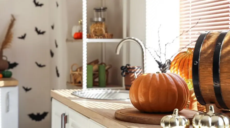 Cozy kitchen with decorative pumpkin, wooden barrel, and sunlight, showcasing autumn decor by The Bosworth Company.