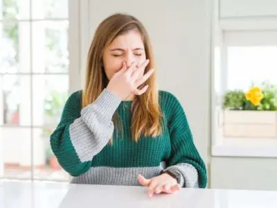 Woman holding her nose, reacting to unpleasant smells indoors, emphasizing the importance of recognizing bad odors from air conditioning systems.