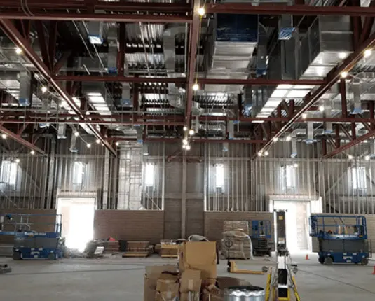 Interior view of the Barbara & George H.W. Bush Convention Center in Midland, Texas, showcasing exposed ductwork and mechanical systems installation, with construction equipment and materials visible on the floor.