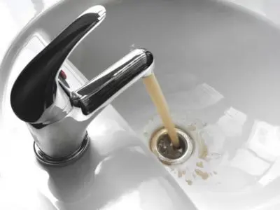 Faucet pouring discolored brown water into a sink, indicating potential pipe corrosion or contamination, relevant to plumbing issues and repiping services.