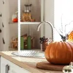 Contemporary kitchen counter with a pumpkin and sink, featuring utensils and a wooden cutting board for home maintenance.