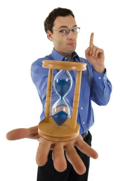 Man in a blue shirt holding an hourglass, symbolizing time management and urgency, relevant to heating service decisions and energy-saving tips.