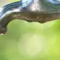 Close-up of an outdoor faucet with water dripping, highlighting plumbing fixtures for summer maintenance.