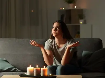 Woman sitting on a couch with candles, expressing concern during a power outage, illustrating the need for standby generators for home safety and convenience.
