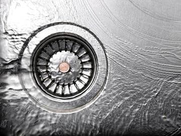 Garbage disposal drain with water flowing, highlighting plumbing maintenance issues and solutions for homeowners.