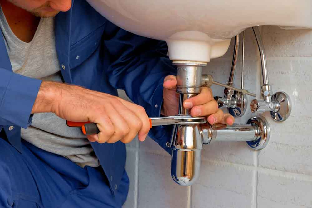 Plumber repairing sink plumbing with wrench, highlighting home maintenance solutions by The Meridian Company.