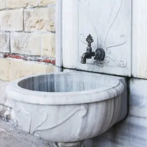 Marble sink with ornate design and vintage faucet against a stone wall, relevant to plumbing services and installations.