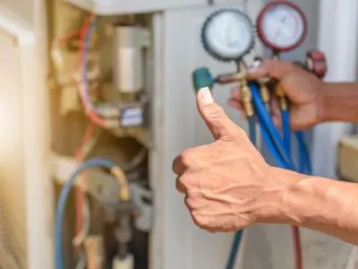 Technician using refrigerant gauges with a thumbs-up gesture, indicating successful refrigerant level adjustment in an air conditioning unit, emphasizing professional HVAC maintenance.
