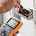 Digital multimeter displaying 235 voltage while inspecting an electrical outlet with red and black wires.