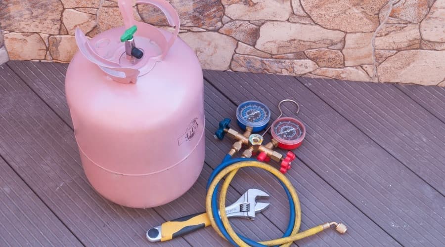 Pink refrigerant tank with pressure gauges and hoses, essential tools for air conditioning maintenance and refrigerant management.