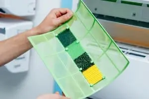 Hand holding a green air filter with multiple colored sections, illustrating HVAC maintenance for improved air quality.