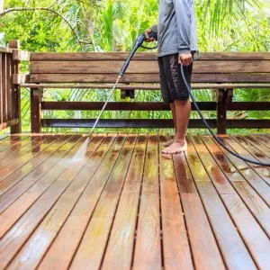 Person using a pressure washer on a wooden deck, highlighting home maintenance and cleaning services relevant to The Meridian Company's offerings.