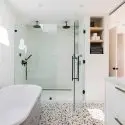 Modern bathroom featuring a white bathtub and glass shower enclosure by The Meridian Company for home improvement.