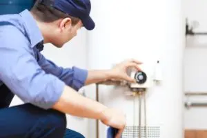 Plumber adjusting settings on a water heater, illustrating maintenance services provided by The Meridian Company.