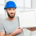 Man in blue hard hat holding a blank frame, showcasing HVAC maintenance tips by The Meridian Company.