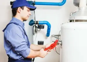 Plumber using adjustable wrench to repair a water heater, highlighting plumbing services by The Meridian Company.