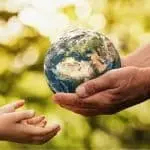 Child's hand reaching for an adult's hand holding a globe, symbolizing environmental responsibility and care for the Earth.