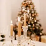Three lit candles next to a Christmas tree, creating a cozy setting for holiday home maintenance with The Meridian Company.