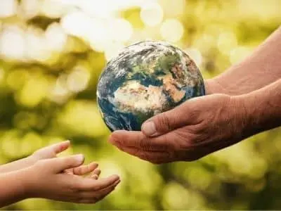 Hands holding a globe symbolizing environmental responsibility and the benefits of green energy for future generations.