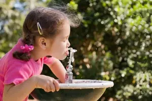 Girl drinking from outdoor water fountain, showcasing plumbing functionality and community access to clean water.