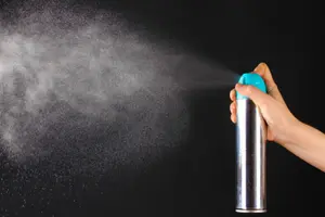 Hand holding a spray can releasing fine mist, illustrating HVAC maintenance solutions for improving indoor air quality.