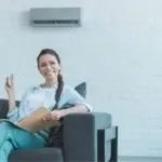Young woman on a sofa using a notepad in a modern room with air conditioning, representing The Meridian Company services.